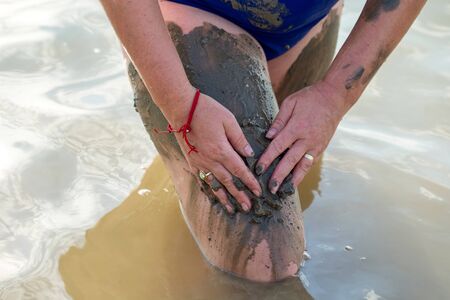 Woman applying on her body salty healing mud in lake