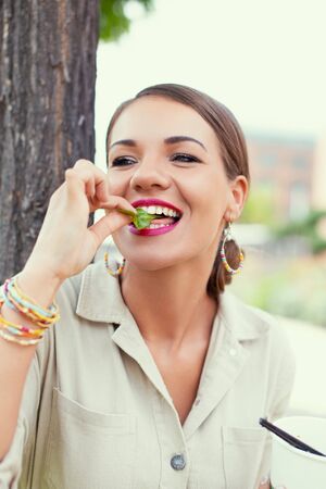 Young Latina woman eating fresh lettuce in public park, dieting at outdoorの写真素材