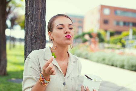 Young Latina woman enjoying eating fresh salad at public park, eyes closedの写真素材