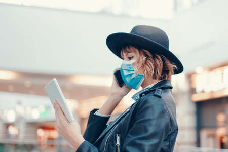 Urban woman in mask using tablet while calling indoors during pandemicの写真素材