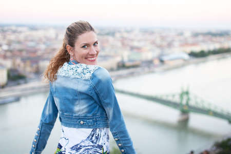 Cheerful 30s urban woman holding hair in Budapest panorama, Hungaryの写真素材