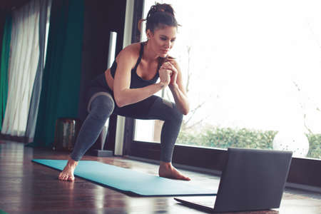 Young Caucasian woman doing squat exercise from online tutorialの写真素材