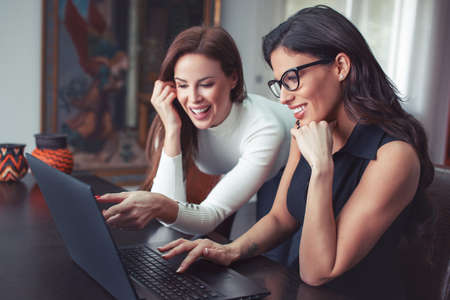 Happy young co-wokers joking at laptop, Caucasian women, online communicationの写真素材