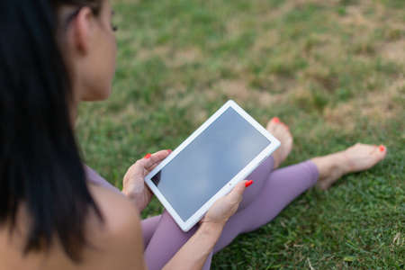 Closeup of young woman in sportswear using digital tablet, sitting on grassの写真素材