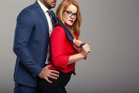 Sexy nerd woman in red holding boss by necktie, seduction