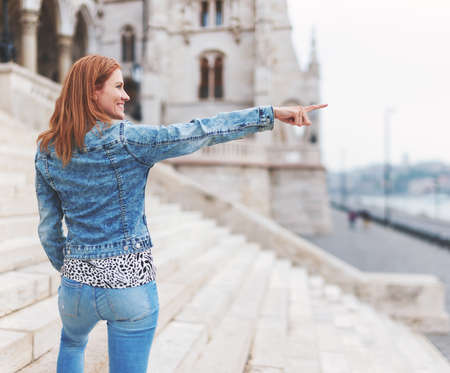 Young redhead hungarian woman pointing into distance at Parliament building, Budapest, Hungaryの写真素材