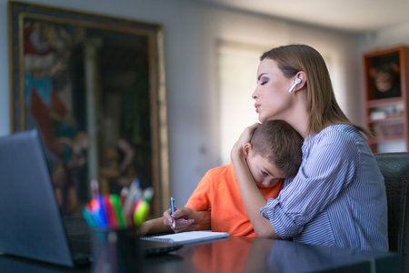 Tired Caucasian mother embracing little son during job at home officeの写真素材