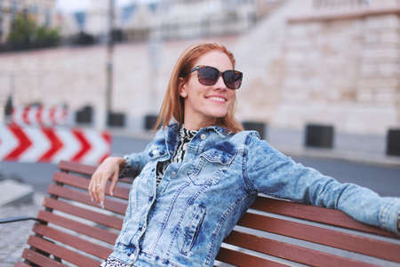 Carefree young redhead urban woman relaxing on bench in cityの写真素材