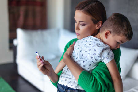 Young worried Caucasian mother watching temperature for little son at homeの写真素材
