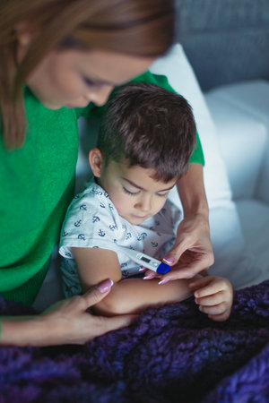 Young Caucasian mother taking temperature under arm for little son at homeの写真素材