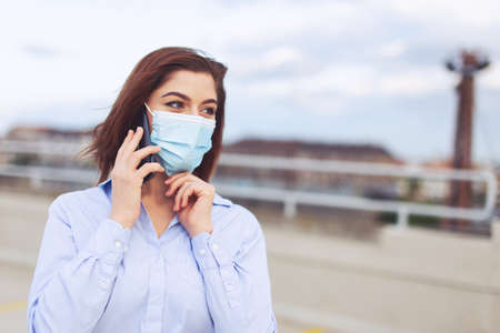Young redhead Caucasian businesswoman in mask calling during pandemic, outdoorsの写真素材