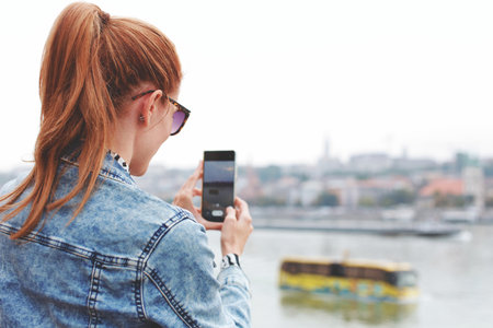 Young redhead woman photographing amphibious city tour bus in river, tourism, city guide