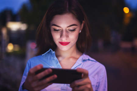 Young redhead Caucasian businesswoman reading news on smartphone at evening in cityの写真素材