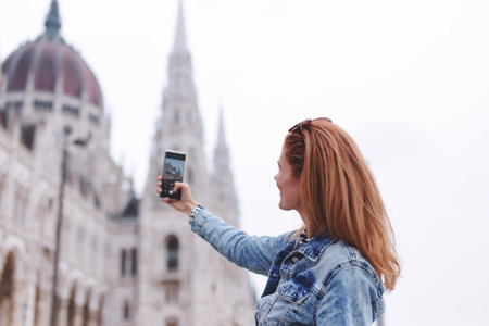 Young redhead woman taking photo of Hungarian Parliament building at Budapest, Hungary