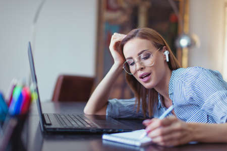 Caucasian univertisy student with hands free device making notes at laptop