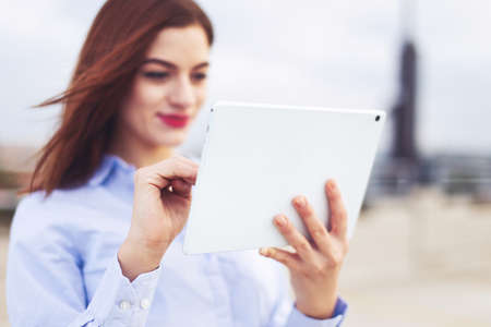Young positive redhead Caucasian businesswoman using tablet outdoors, depth of fieldの写真素材
