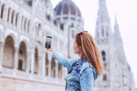 Young redhead Caucasian woman taking photo of Hungarian Parliament building at Budapest, Hungaryの写真素材