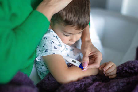 Mother taking temperature to little son at home closeup