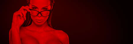 Sexy nerd woman in red light holding eyeglasses bannerの写真素材