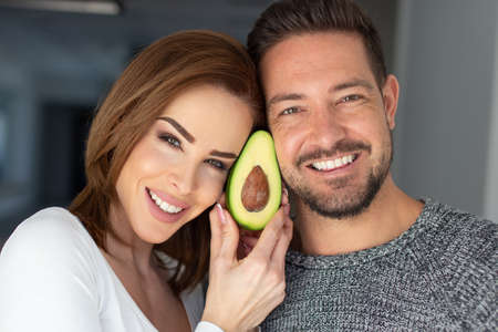 Happy young Caucasian couple holding avocado at face portraitの写真素材