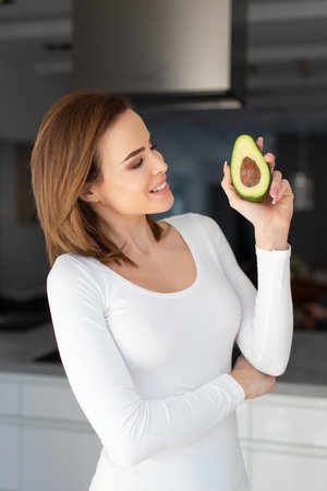 Young 30s Caucasian woman showing avocado at kitchen