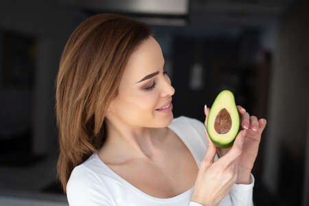 Young Caucasian woman turning and holding halved avocado