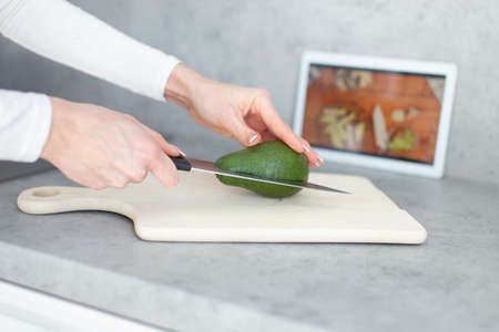 Woman hands halving avocado on cutting board, online cooking tutorialの写真素材