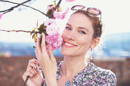 Happy young woman holding cherry tree blossom with toothy smile at springtime, sakuraの写真素材