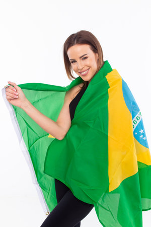 Happy young woman covering herself with Brazilian flag on white backgroundの写真素材