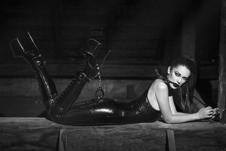 Sexy young woman lays on timber with whip in mouth at night black and whiteの写真素材