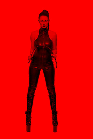 Sexy caucasian dominatrix in latex catsuit bending whip in red lightの写真素材