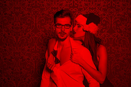 Sexy santa woman undress man at Christmas in red light, foreplayの写真素材