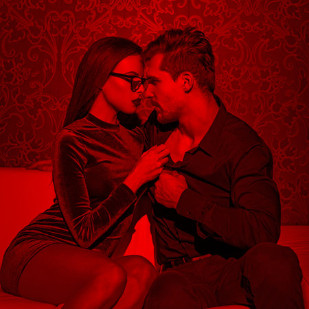 Sexy young woman undressing rich man shirt in club in red lightの写真素材