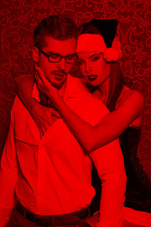 Sexy santa woman seduces young man in tux at Christmas in red lightの写真素材