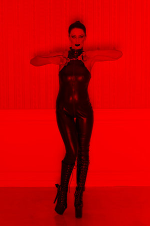 Brunette sexy woman in latex catsuit showing handcuffs in red light, bdsmの写真素材