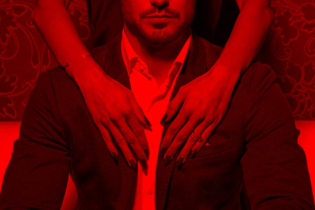 Sexy woman hands with red nails embrace rich man in red lightの写真素材