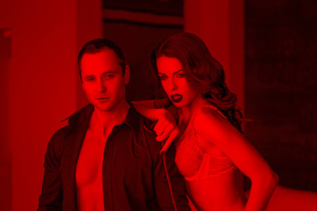 Macho man posing with sexy dominatrix indoors, bdsm in red lightの写真素材