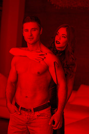 Sexy confident macho man with dominatrix and whip indoors in red light, bdsmの写真素材