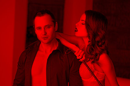 Sexy dominant woman posing with rich macho man in red lightの写真素材