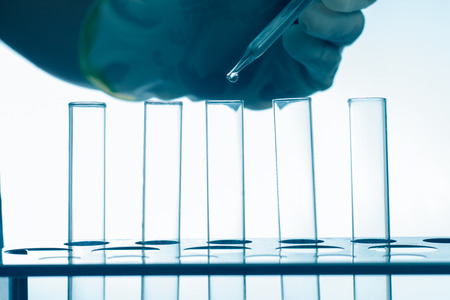 Pipette adding fluid in to test tubes,blue style background