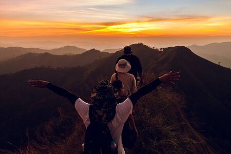 Rear view of four backpacker walking in path on mountain at sunsetの写真素材