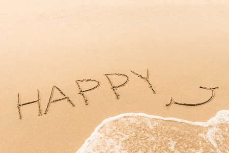 Handwriting words "Happy " with soft wave on sand at beach backgroundの写真素材