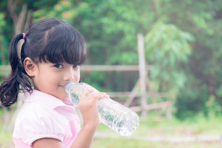 asian little girl drinking water in the forestの写真素材