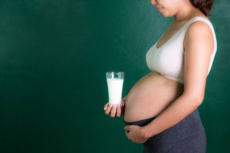 asian pregnant woman holding a glass of milk with green background.の写真素材