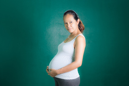 Pregnant woman touching belly with green concrete wall backgroundの写真素材