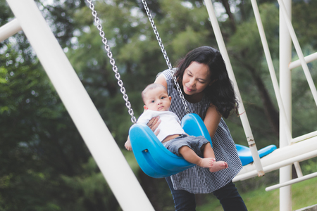 mother playing swing with  baby on  playground.の写真素材