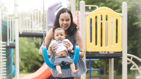 mother playing swing with  son baby on  playground.の写真素材