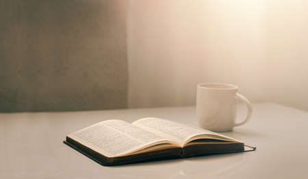 Open a bible by the window with a cup of coffee for the morning light. and put it on a wooden table...
