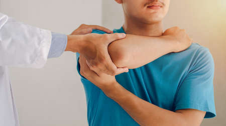 Doctors or physical therapists work to treat the injured arm of a male patient who has performed...