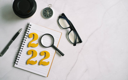 new year 2022 on desk 2022 goals with notebook, coffee cup, magnifying glass and glasses on wooden...